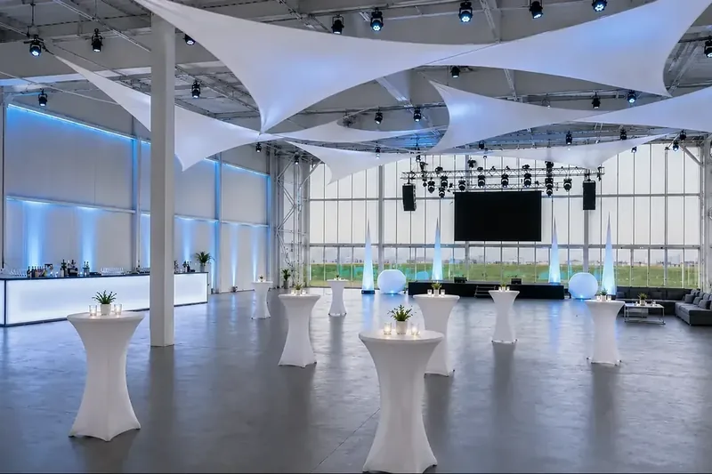 Hell und festlich eingedeckter Hangar mit Lichtsegeln und großen Tafeln
