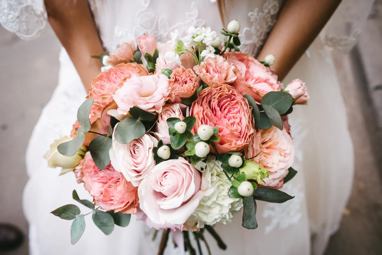 Brautstrauß aus rosa Rosen, Nelken und Eukalyptus in den Händen der Braut
