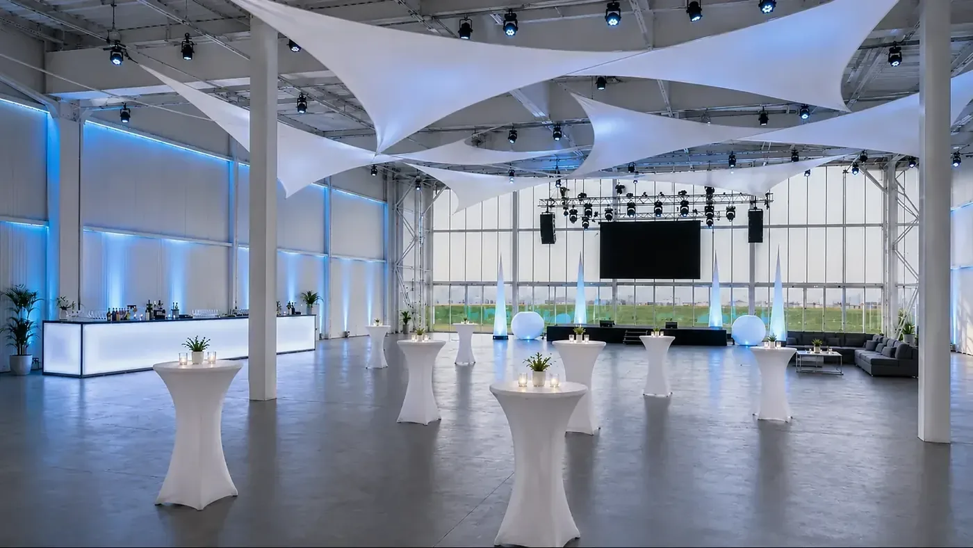 Hell und festlich eingedeckter Hangar mit Lichtsegeln und großen Tafeln bei aircraft events