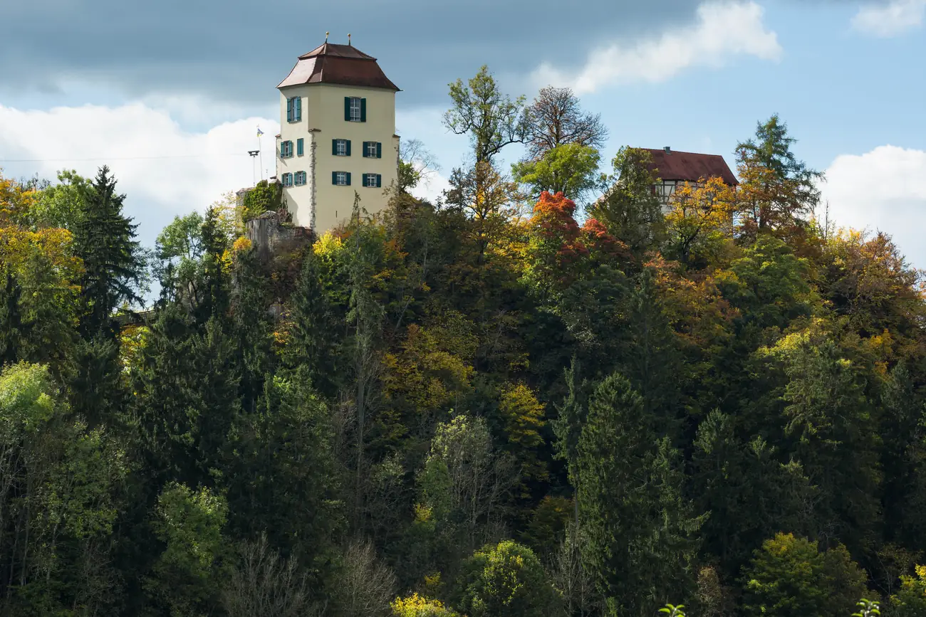 Schloss auf einem bewaldeten Felssporn über dem Donautal, umgeben von herbstlich gefärbten Bäumen
